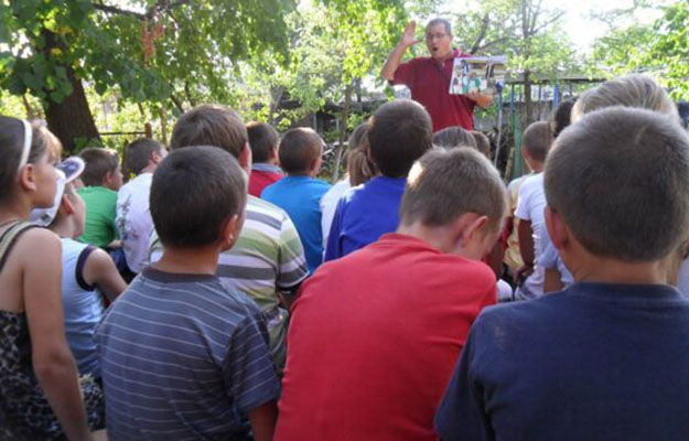 Eine Kindergruppe von hinten, der von einem Mann eine Geschichte erzählt wird.