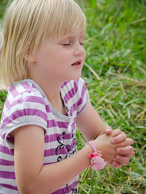 Ein kleines Kind auf einer Wiese welches betet.