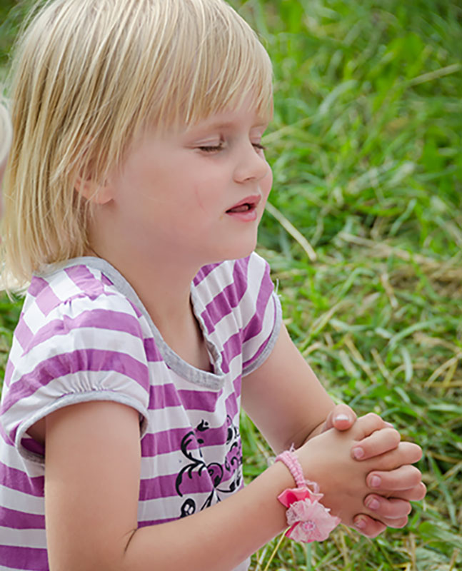 Ein kleines Kind auf einer Wiese welches betet.